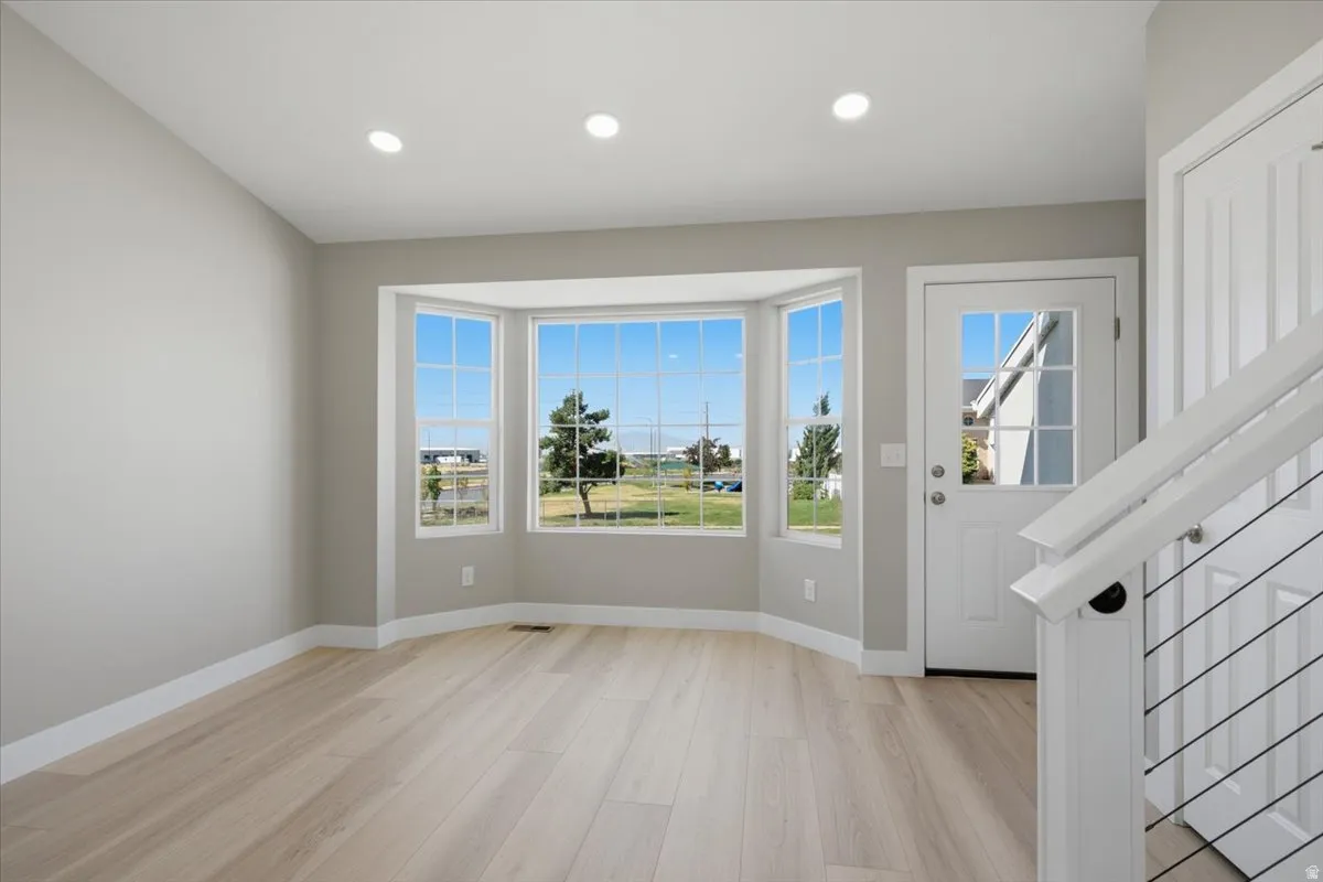 Spacious room featuring a bay window with multiple panes, recessed lighting, light wood-finish flooring, and a white entry door with glass inserts