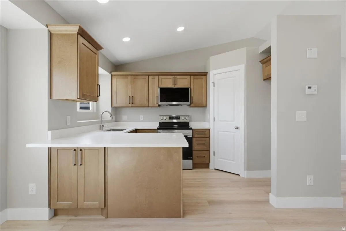 Modern kitchen featuring light wood-finish cabinetry, white countertops, and stainless steel appliances