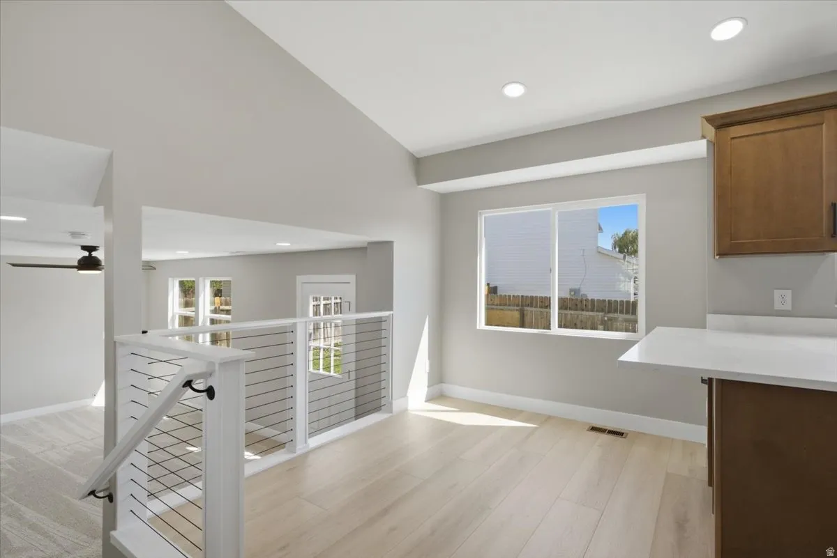 Open concept living space featuring light wood-finish flooring, recessed lighting, white cable railing, and a kitchen counter with a white surface