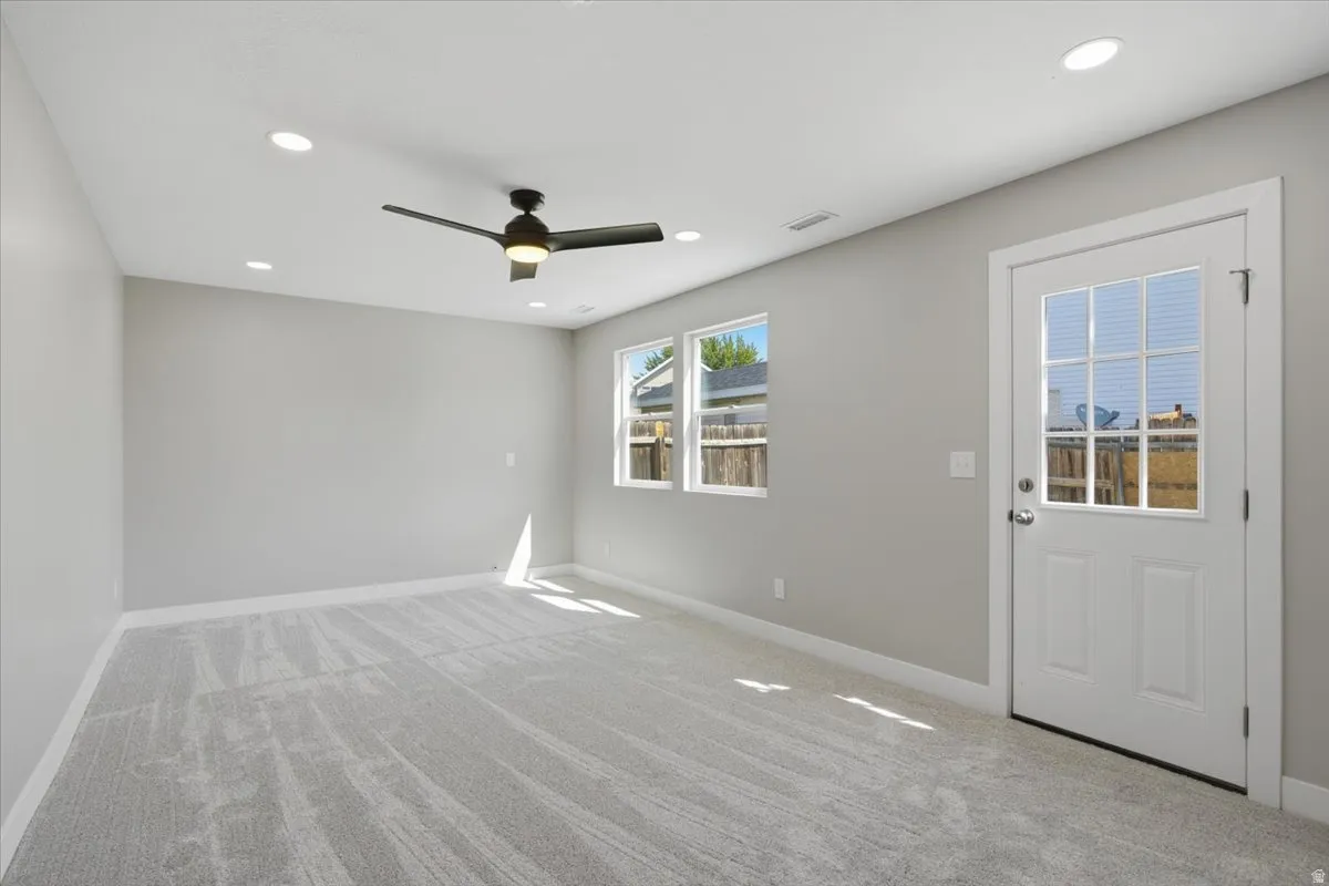 Spacious room featuring light gray carpeting, recessed lighting, a ceiling fan, multiple windows, and a glass-paneled exterior door
