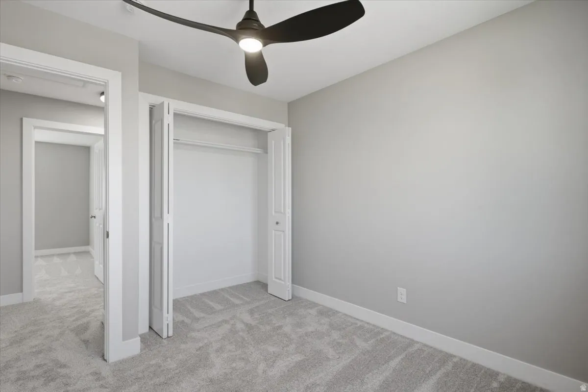 Bedroom featuring light gray wall paint, gray patterned carpet, a ceiling fan with integrated lighting, and a closet with bifold doors