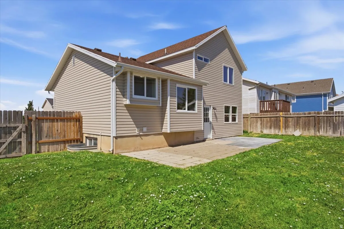 Rear exterior featuring light-colored horizontal siding, multiple windows, and a concrete patio