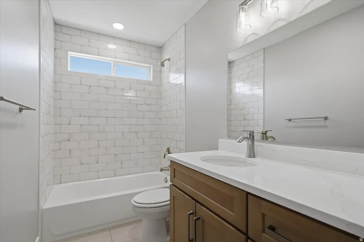 Bathroom featuring a white subway tile shower surround with a horizontal window, light wood-finish vanity with a white countertop and integrated sink, and brushed nickel fixtures