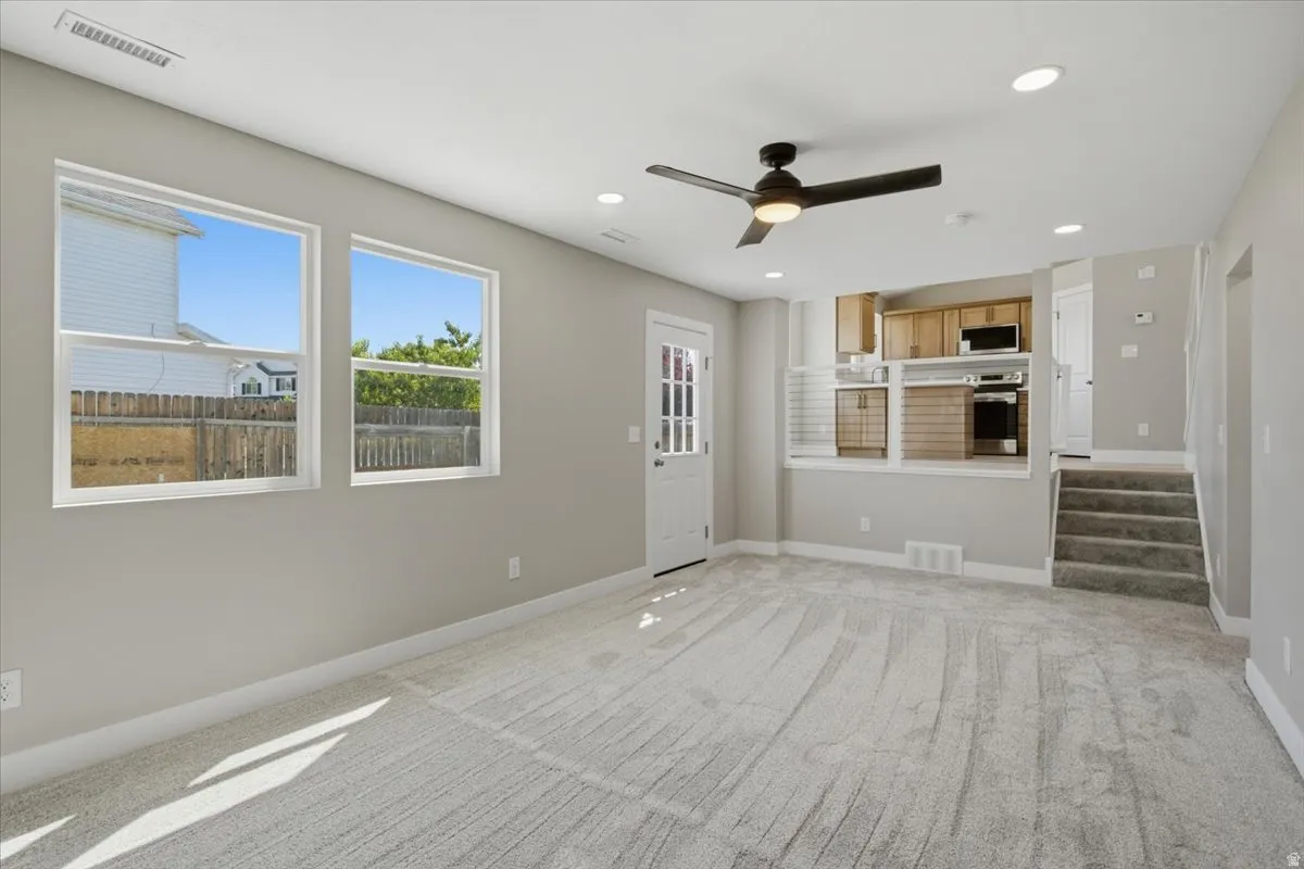 Open concept living area featuring light gray walls, plush carpet flooring, a ceiling fan with integrated lighting, recessed ceiling lights, and two windows
