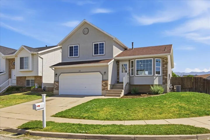 Two-story stucco and stone veneer residence featuring an attached garage, bay window, front porch with white railing, and a mature front lawn