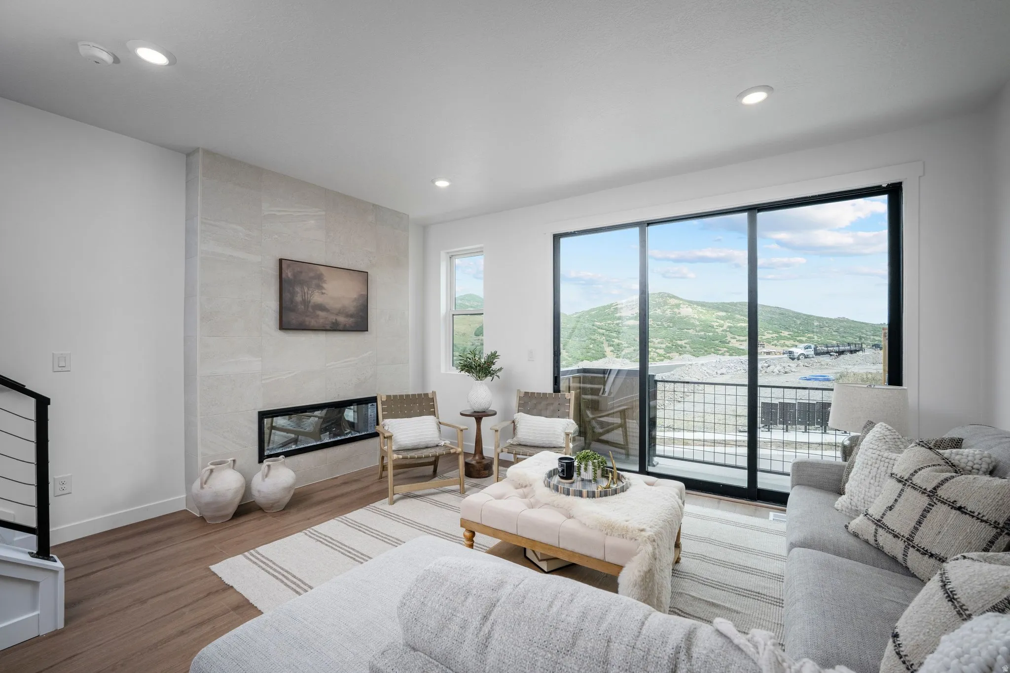 Spacious living area featuring floor-to-ceiling sliding glass doors, a linear fireplace set into a large-format tile surround, recessed lighting, and wood-finish flooring
