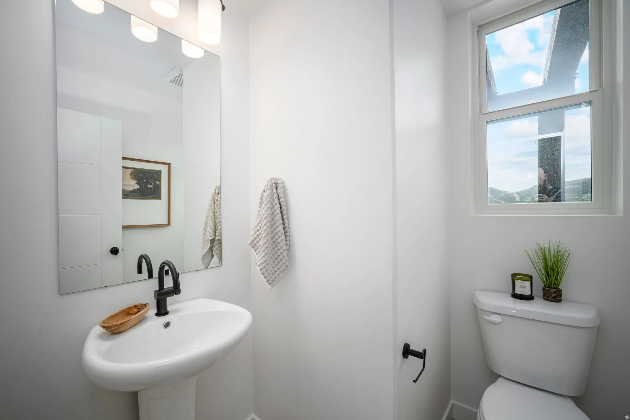Modern bathroom featuring a pedestal sink with a matte black faucet, a large vanity mirror, built-in storage cabinetry, a toilet, and an operable window
