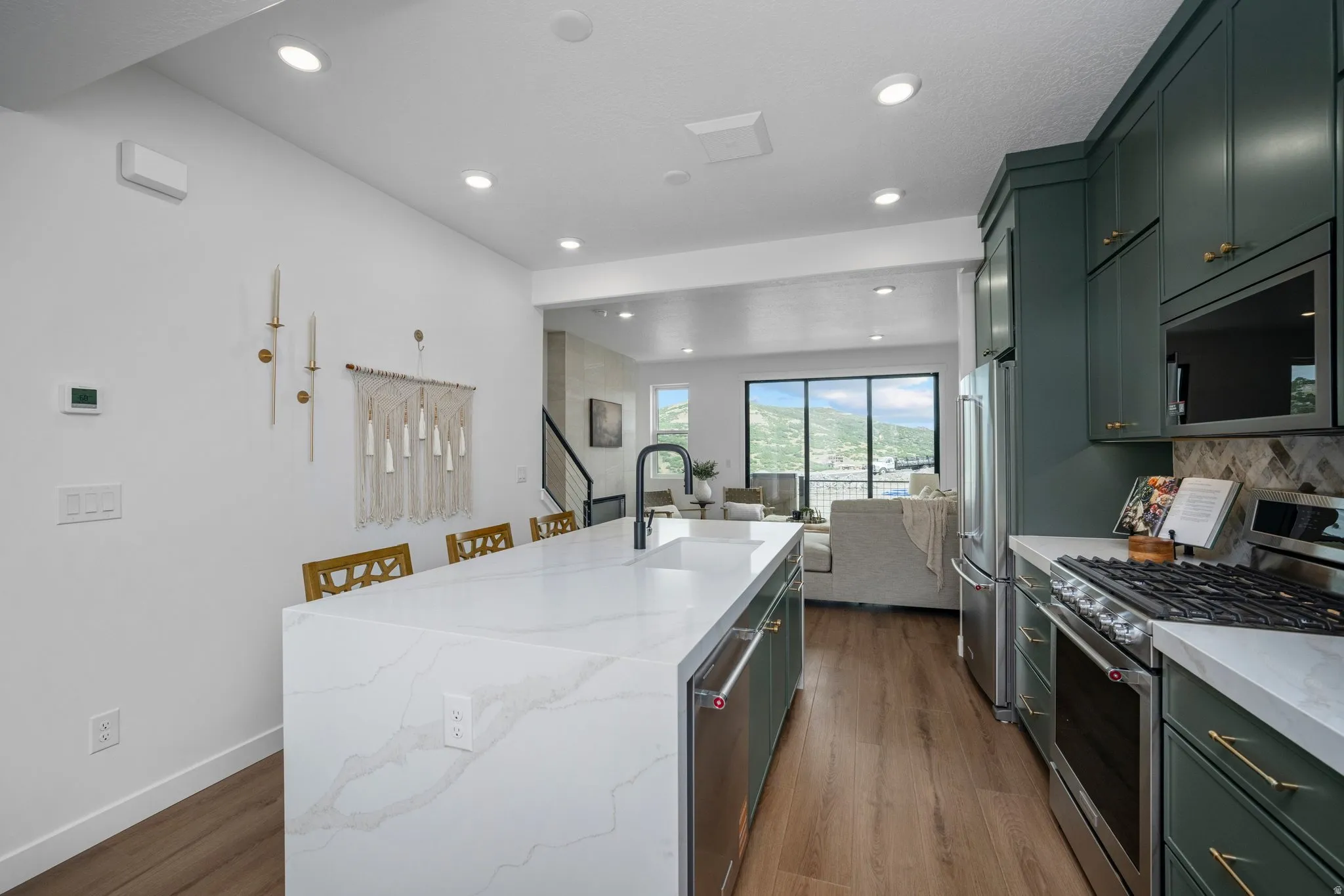 Kitchen featuring a waterfall island with an integrated sink, dark green cabinetry, stainless steel appliances, and wood-finish flooring
