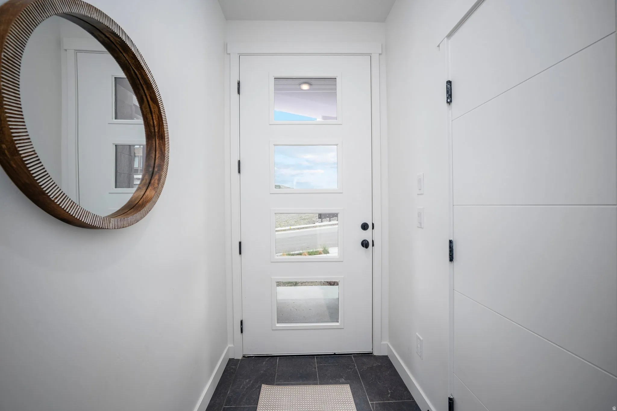 Entryway featuring a white door with rectangular glass inserts, dark tile flooring, and white baseboards
