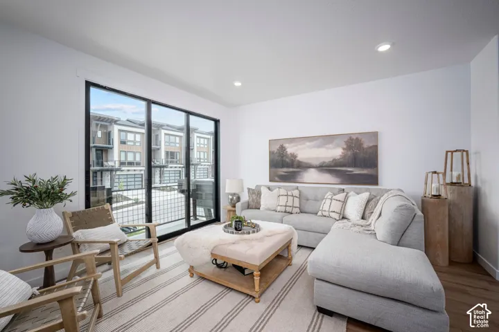 Living area featuring large format sliding glass doors with black framing, recessed lighting, and wood-finish flooring