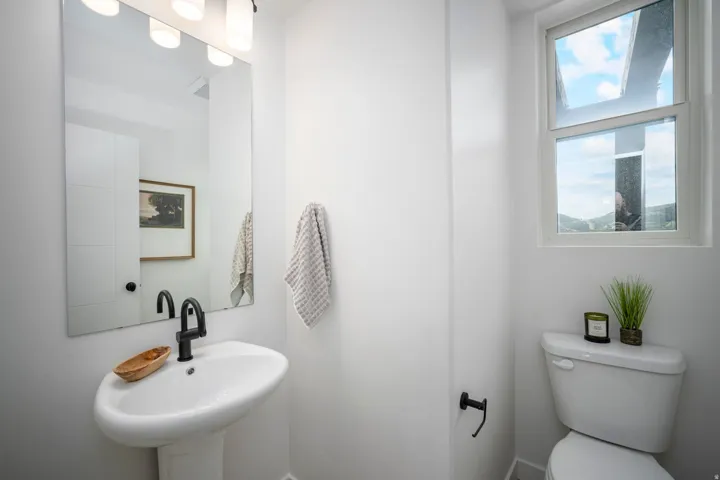 Modern bathroom featuring a pedestal sink with a matte black faucet, a large vanity mirror, built-in storage cabinetry, a toilet, and an operable window