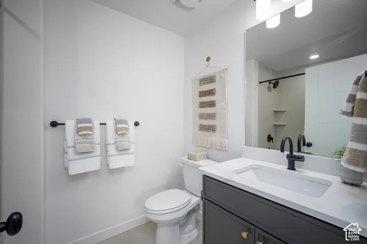 Bathroom vanity featuring a single basin sink, white countertop, and dark cabinetry with gold-tone hardware