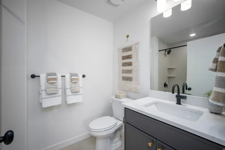 Bathroom vanity featuring a single basin sink, white countertop, and dark cabinetry with gold-tone hardware