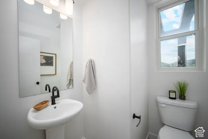 Modern bathroom featuring a pedestal sink with a matte black faucet, a large vanity mirror, built-in storage cabinetry, a toilet, and an operable window