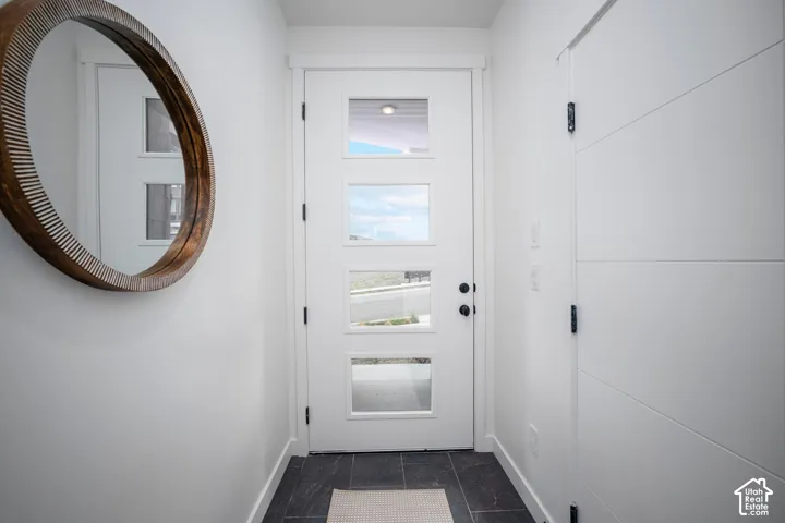 Entryway featuring a white door with rectangular glass inserts, dark tile flooring, and white baseboards