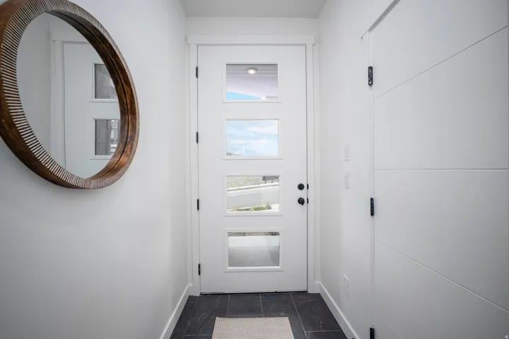 Entryway featuring a white door with rectangular glass inserts, dark tile flooring, and white baseboards