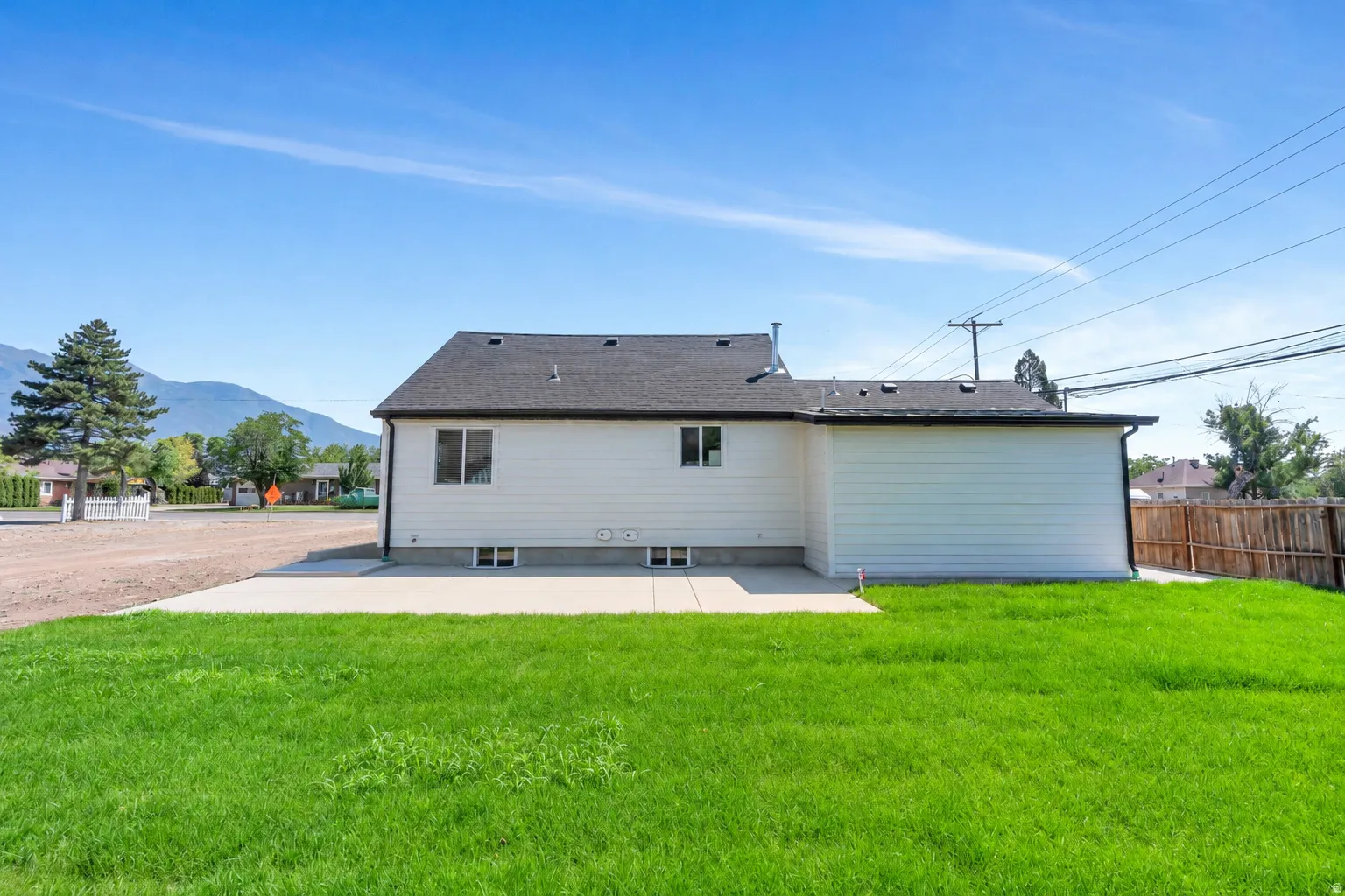 Expansive green lawn with a concrete patio, white horizontal siding, dark shingle roof, and a partial wood fence