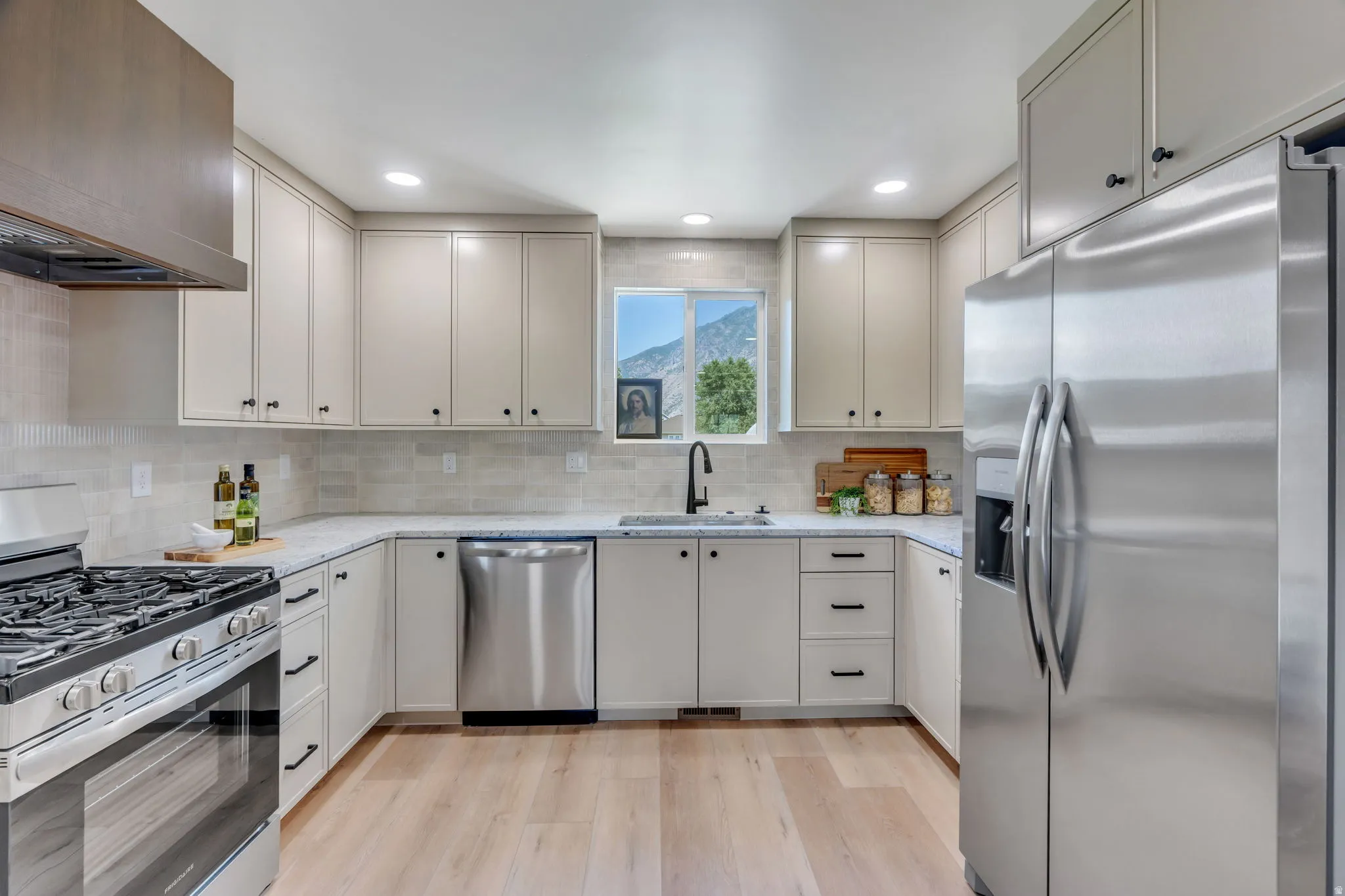 Modern kitchen featuring light wood-finish flooring, stainless steel appliances, light-toned cabinetry with dark hardware, quartz countertops, and a subway tile backsplash