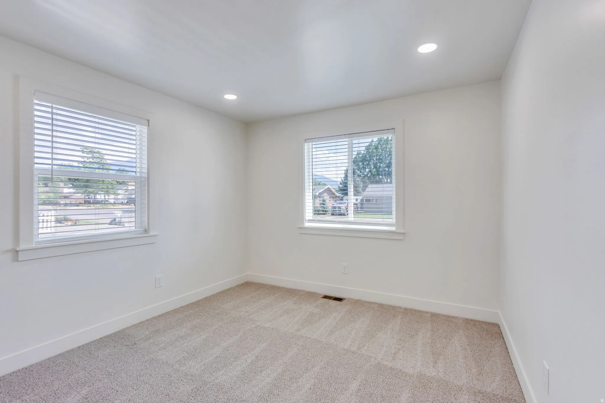 Spacious room featuring neutral carpeting, recessed ceiling lighting, two windows with blinds, and white trim throughout