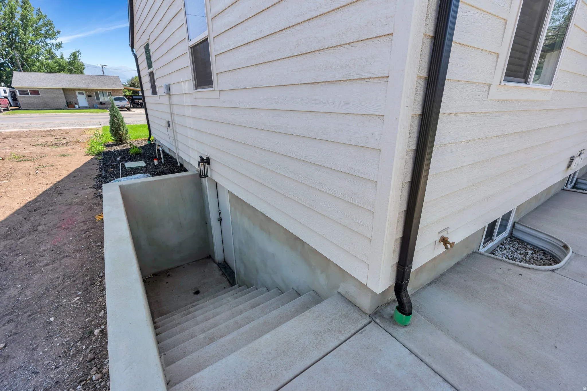 Exterior features light-colored horizontal siding, a dark downspout, and a concrete basement entry with stairs