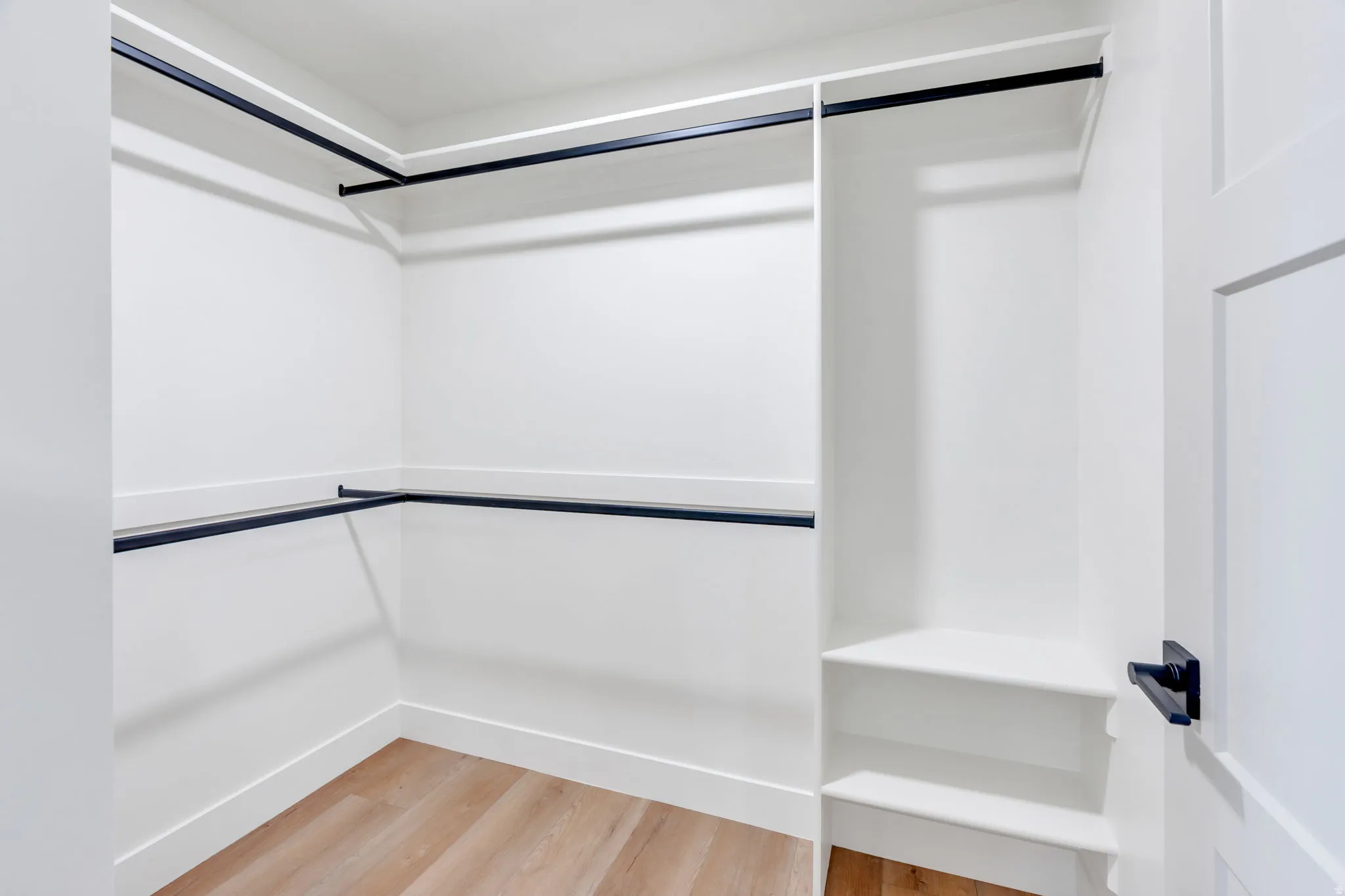 Spacious closet featuring multiple hanging rods, integrated shelving, light wood-finish flooring, and a crisp white color palette