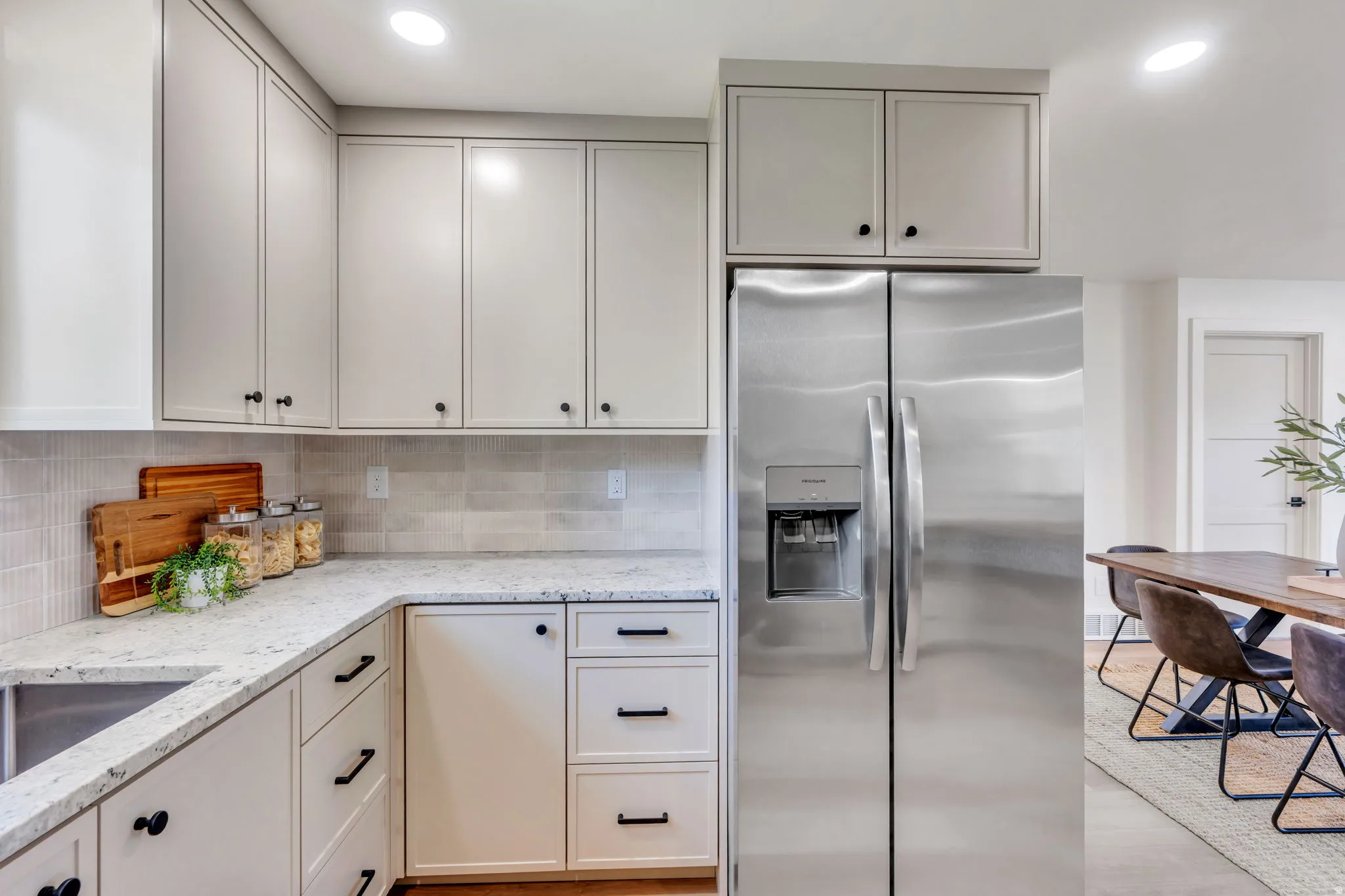 Contemporary kitchen featuring light-toned cabinetry, stainless steel side-by-side refrigerator, white speckled countertops, and a subway tile backsplash