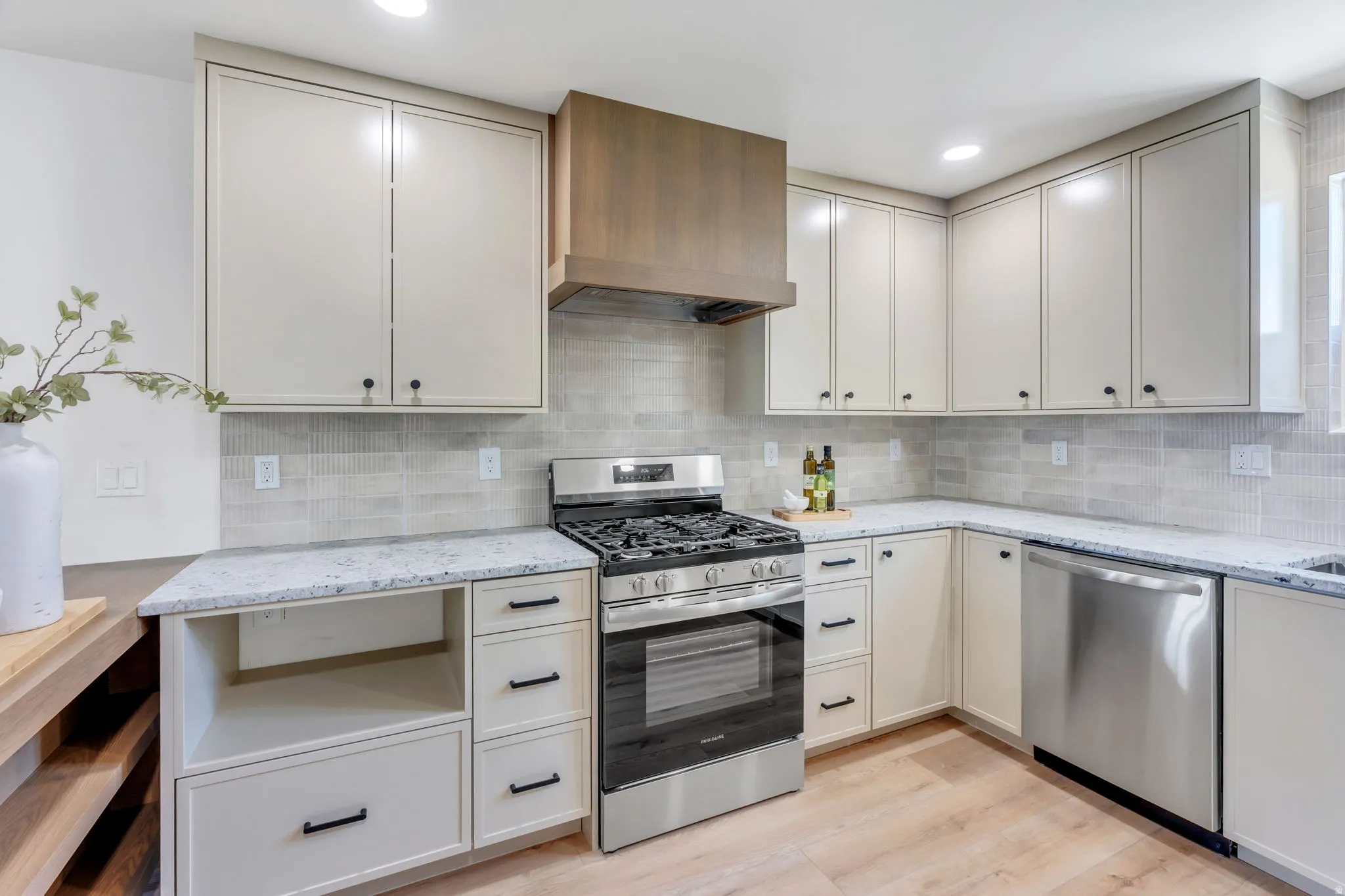 Modern kitchen featuring light-toned cabinetry, stainless steel appliances, speckled countertops, a tile backsplash, and wood-finish flooring
