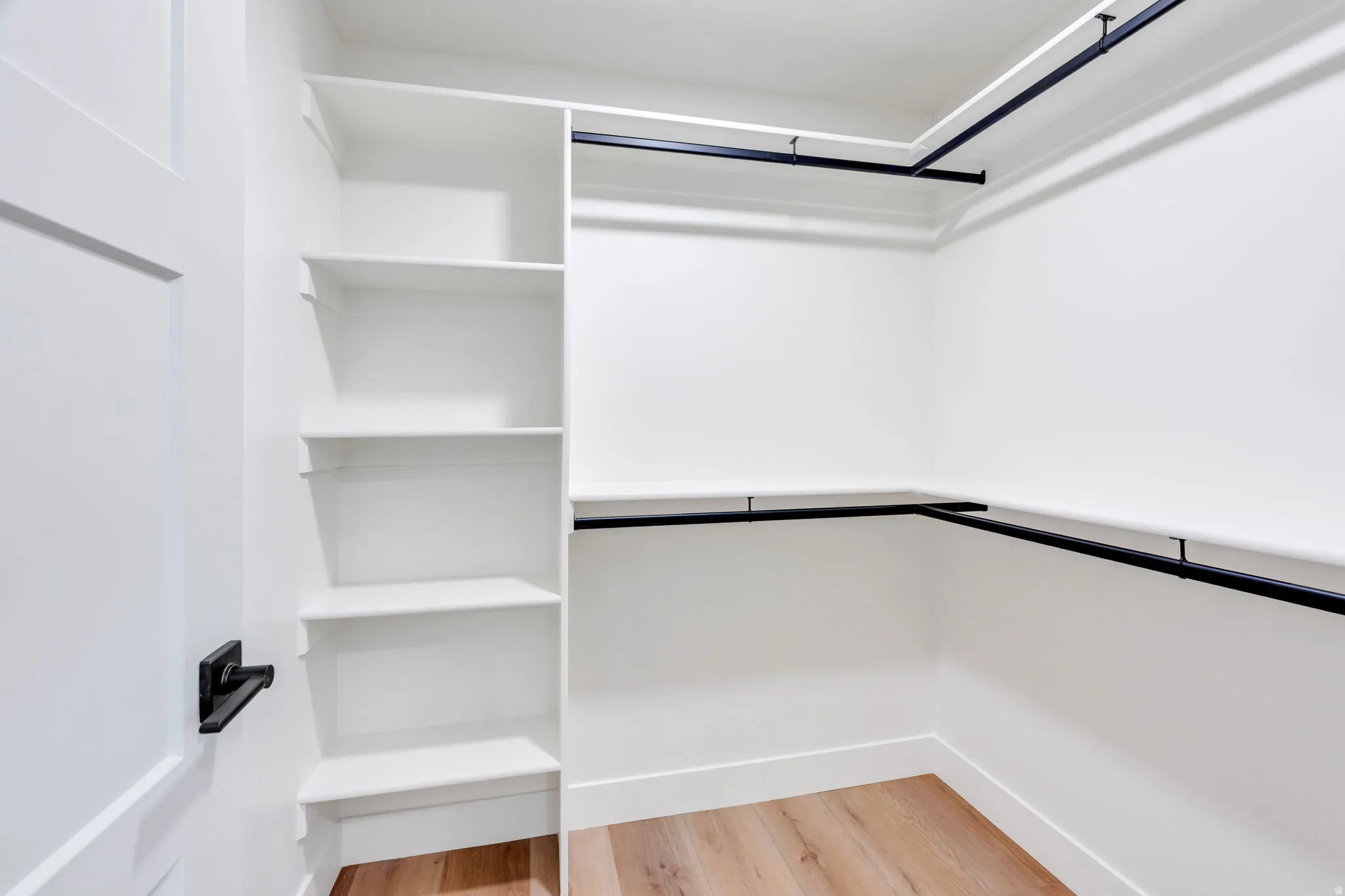 Walk-in closet featuring built-in shelving, black hanging rods, white walls, and wood-finish flooring