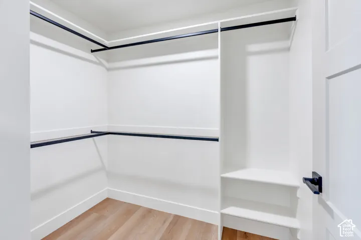 Spacious closet featuring multiple hanging rods, integrated shelving, light wood-finish flooring, and a crisp white color palette