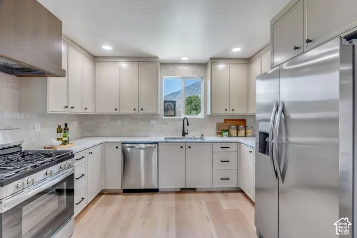 Modern kitchen featuring light wood-finish flooring, stainless steel appliances, light-toned cabinetry with dark hardware, quartz countertops, and a subway tile backsplash