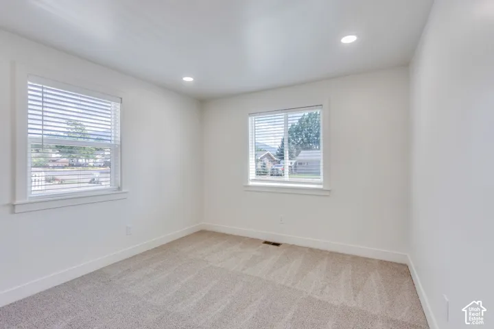 Spacious room featuring neutral carpeting, recessed ceiling lighting, two windows with blinds, and white trim throughout