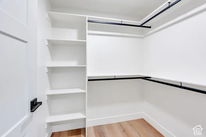 Walk-in closet featuring built-in shelving, black hanging rods, white walls, and wood-finish flooring