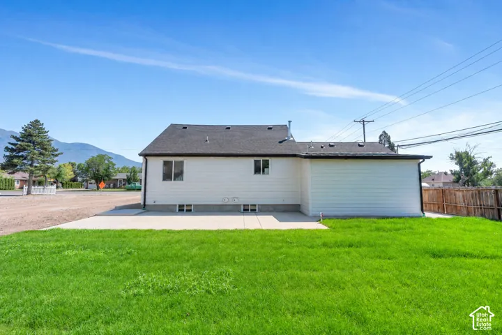 Expansive green lawn with a concrete patio, white horizontal siding, dark shingle roof, and a partial wood fence