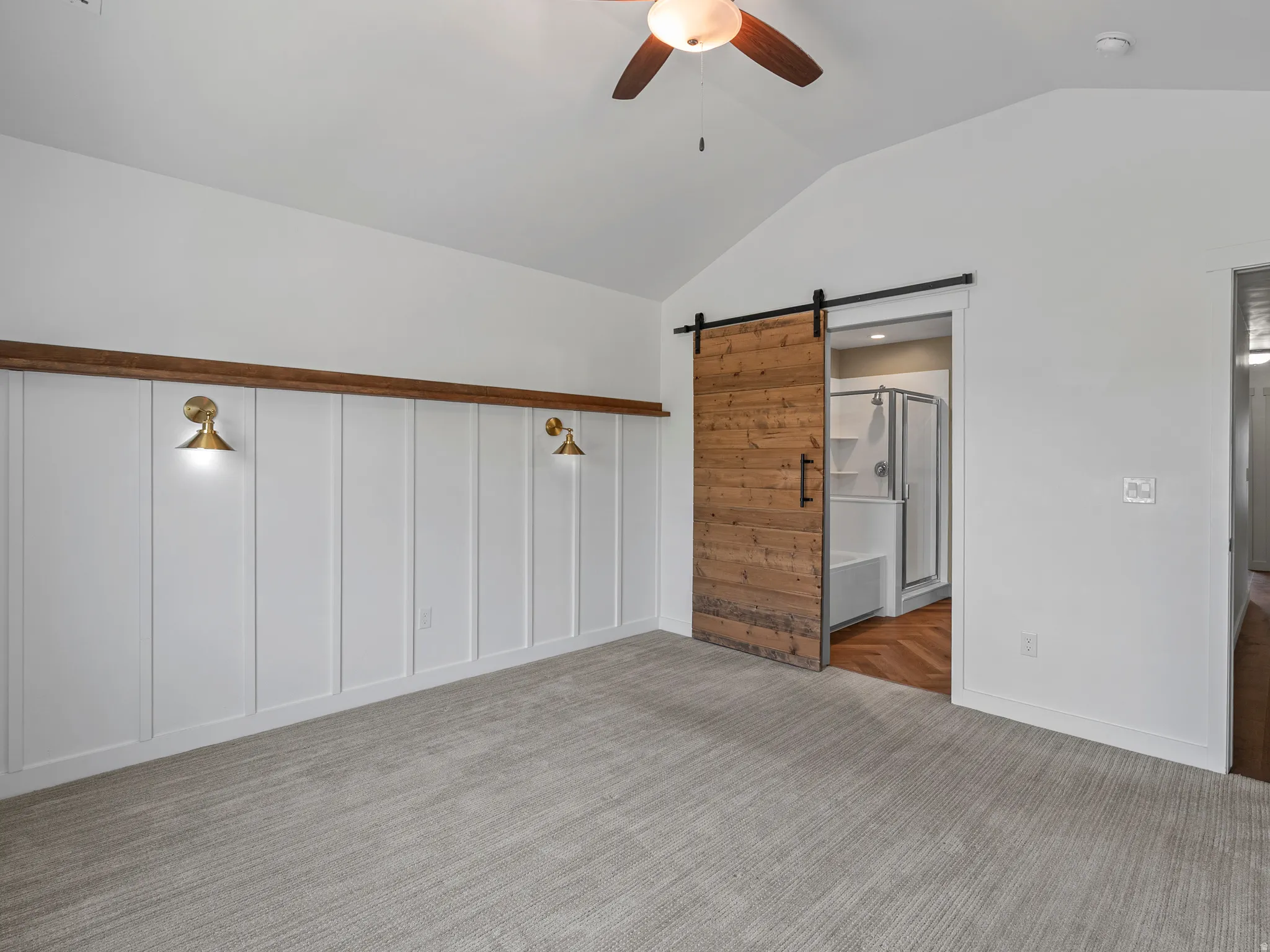 Spacious room featuring vaulted ceilings, a wood-finish barn door, and a board and batten accent wall with brass sconces