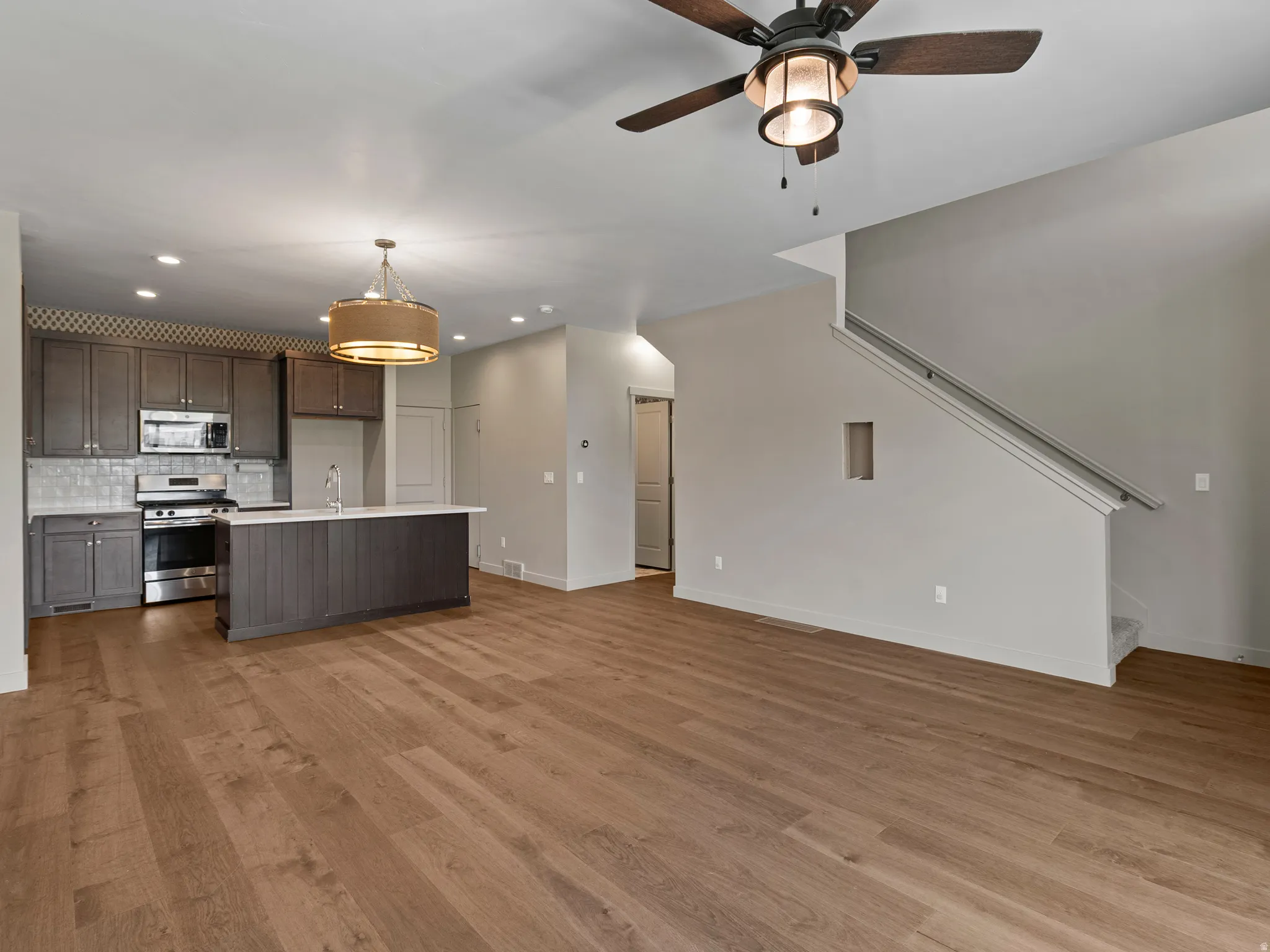 Open-concept living and kitchen area featuring wood-finish flooring throughout, recessed lighting, and a ceiling fan with integrated light fixture