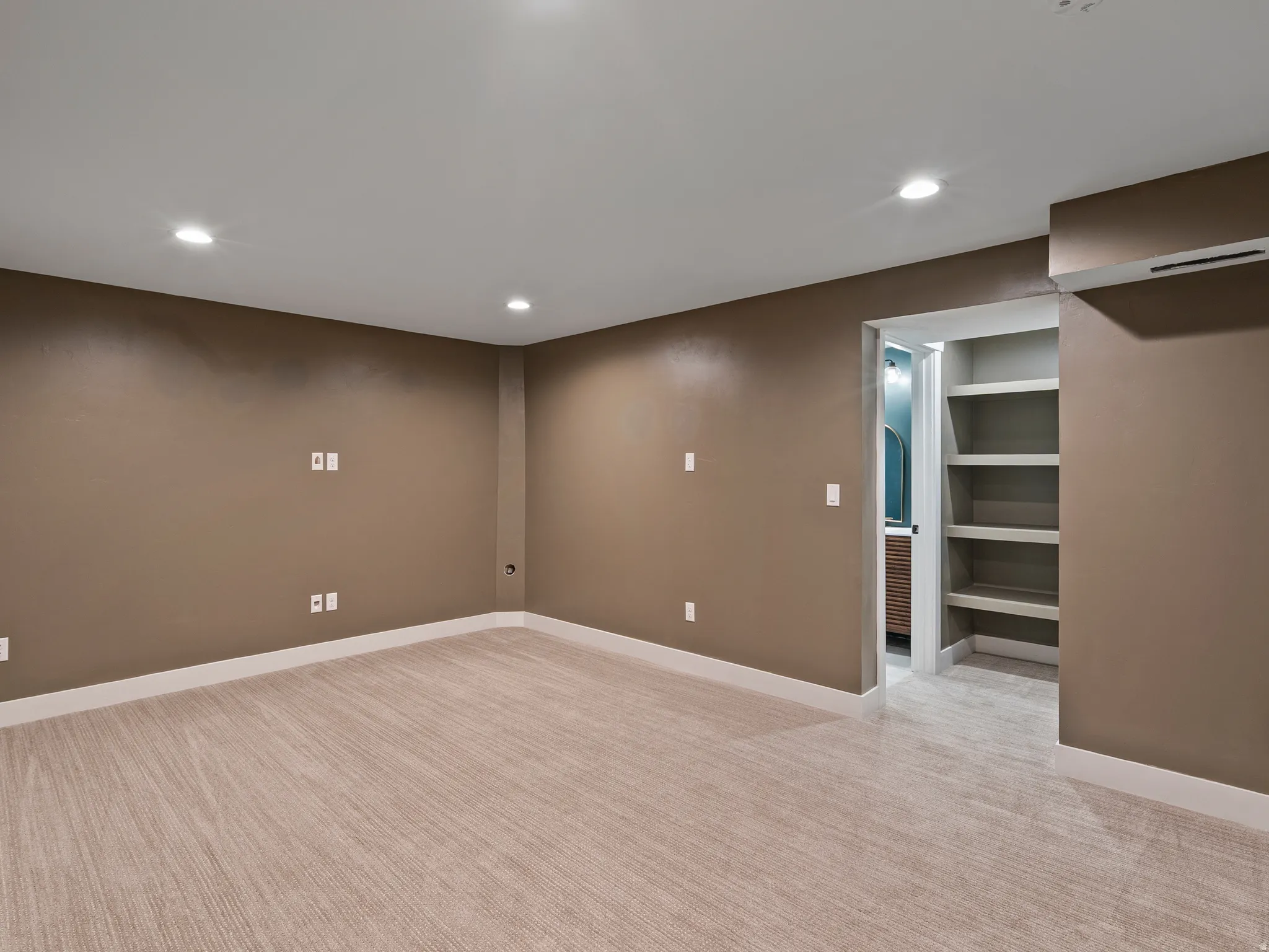 Spacious recreational room featuring neutral taupe walls, recessed ceiling lighting, and wide-plank wood-finish flooring throughout