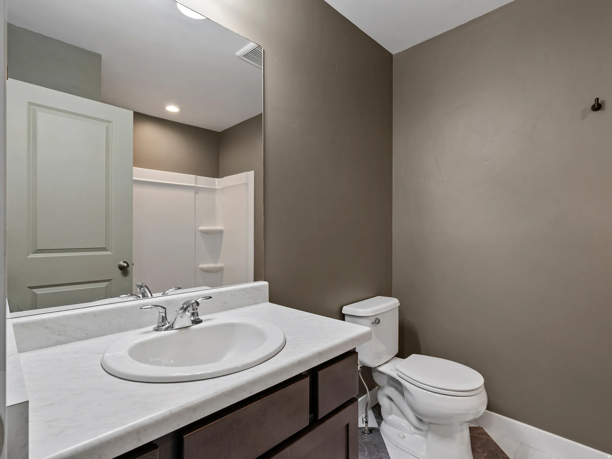 Modern bathroom featuring a round ceramic sink set atop a white marble countertop with dark wood cabinetry, chrome two-handle faucet, and large framed mirror with integrated lighting