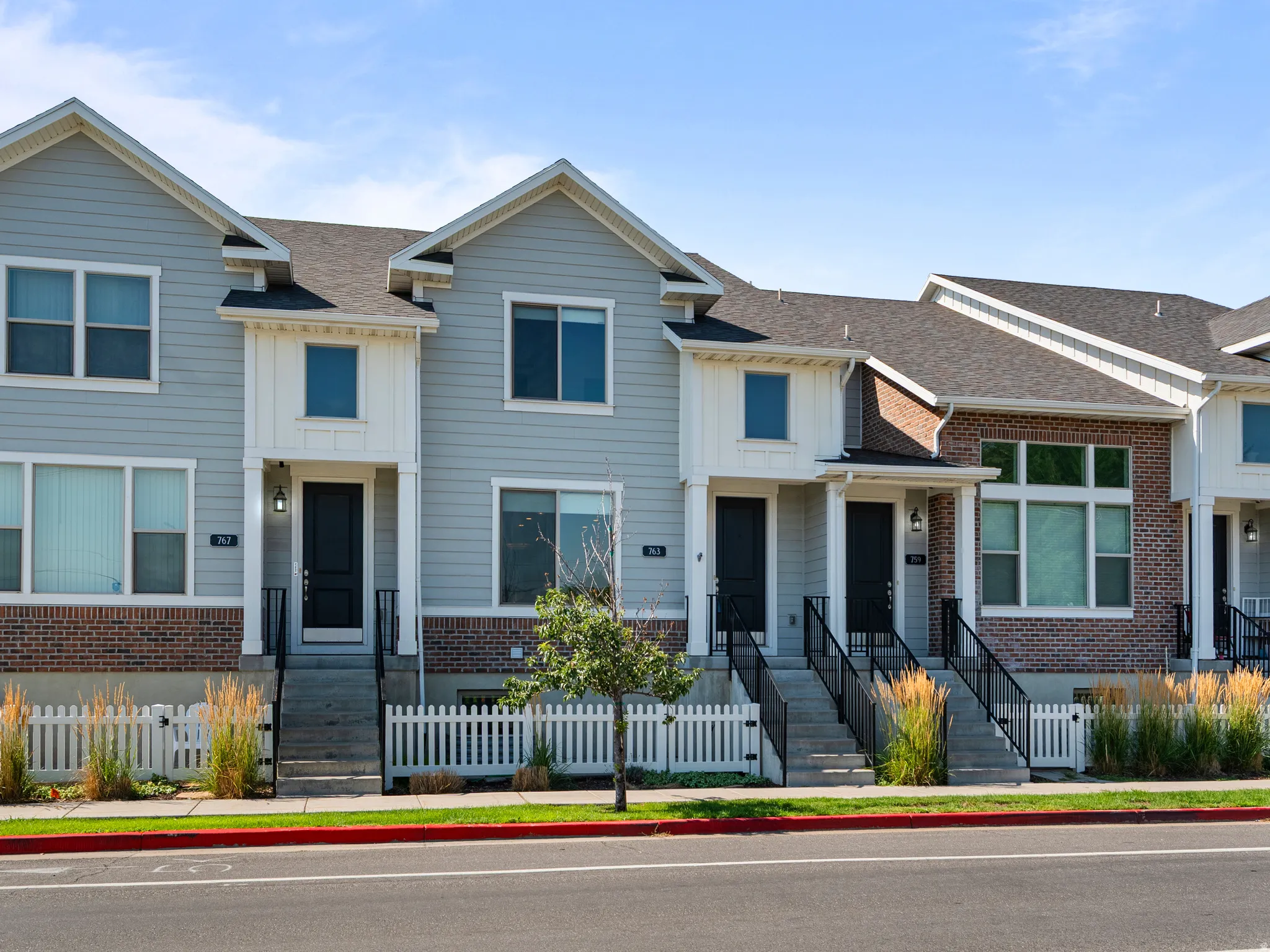 Contemporary townhome exterior featuring light gray siding, dark brick accents, and a dark asphalt shingle roof