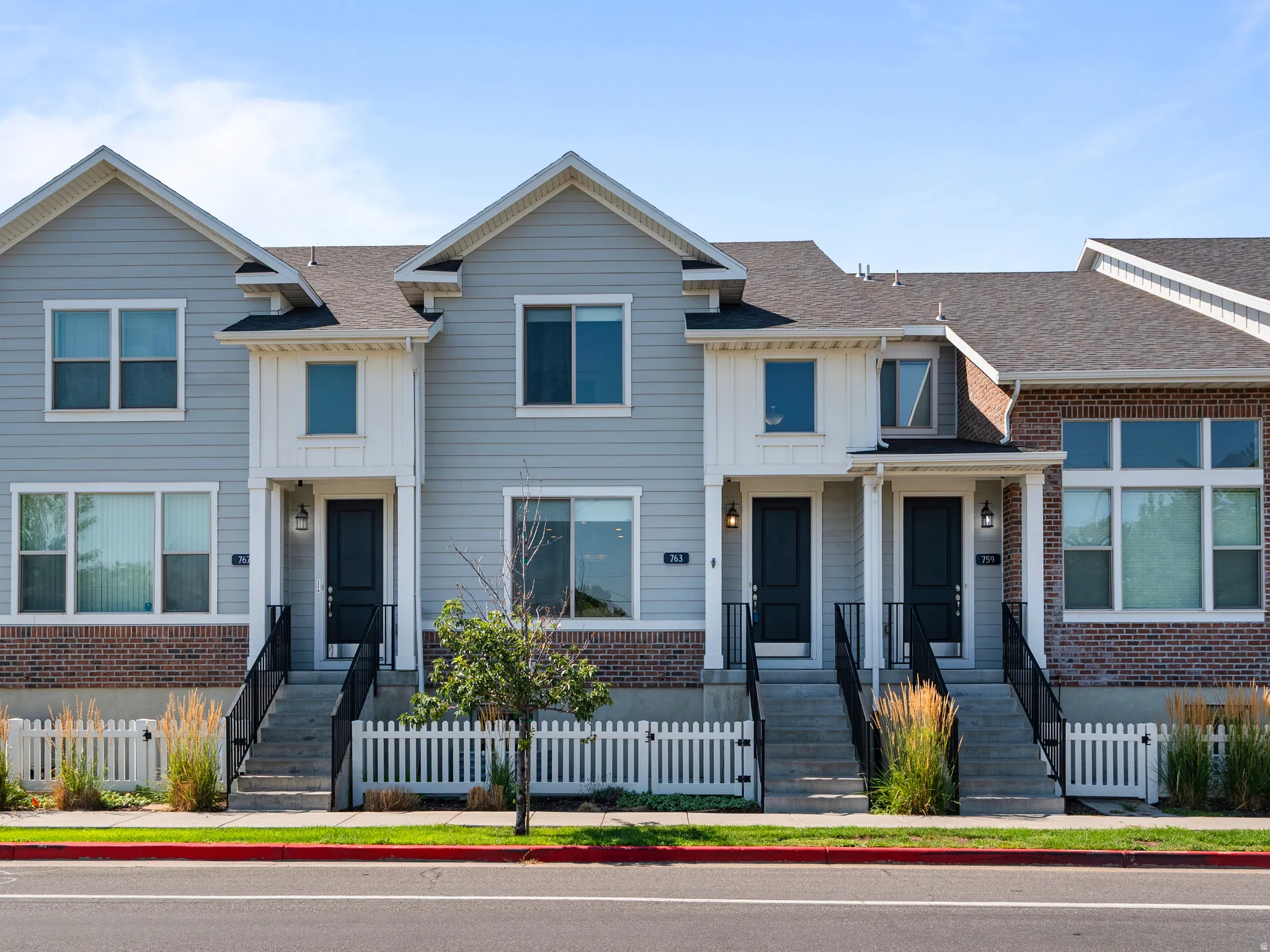Modern townhome exterior featuring light gray siding, dark gray roofing, and a brick base
