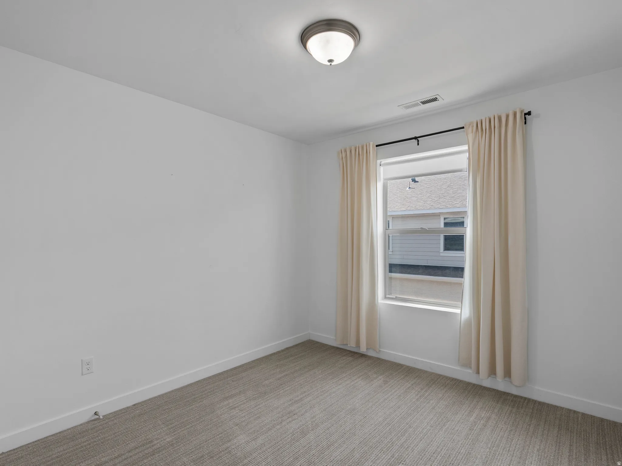 Bedroom featuring a window with a curtain rod and drapes, neutral-toned carpeting, white walls, and a flush-mount ceiling light fixture