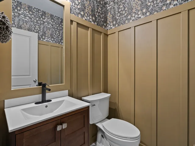 Elegant half bath featuring a white ceramic sink with oil-rubbed bronze faucet mounted on a wood-finish vanity, white porcelain toilet, and neutral wall paneling