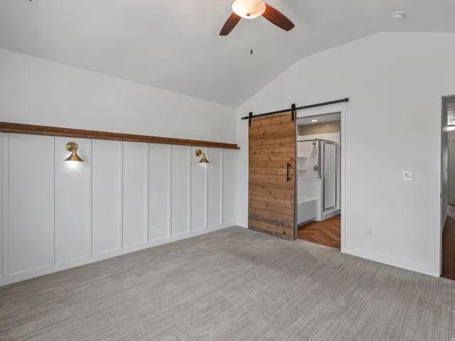 Spacious room featuring vaulted ceilings, a wood-finish barn door, and a board and batten accent wall with brass sconces