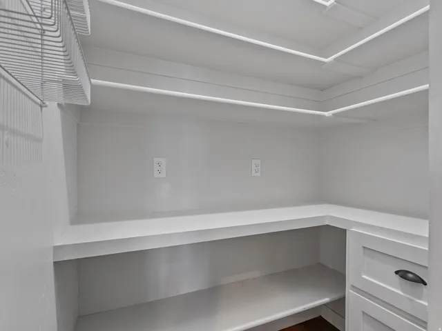 Pantry with built-in shelving, wire rack storage, multiple electrical outlets, and cabinetry with dark hardware