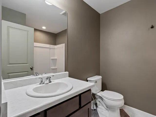 Modern bathroom featuring a round ceramic sink set atop a white marble countertop with dark wood cabinetry, chrome two-handle faucet, and large framed mirror with integrated lighting