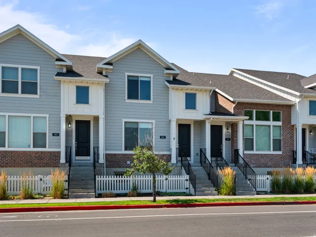 Contemporary townhome exterior featuring light gray siding, dark brick accents, and a dark asphalt shingle roof