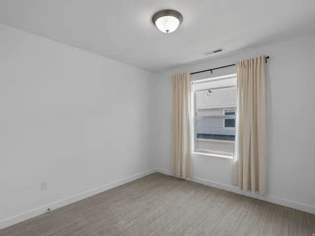 Bedroom featuring a window with a curtain rod and drapes, neutral-toned carpeting, white walls, and a flush-mount ceiling light fixture