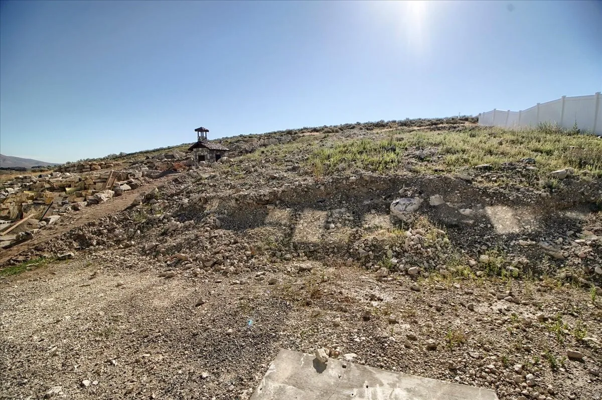 Sloping hillside lot with partial white fence along the perimeter