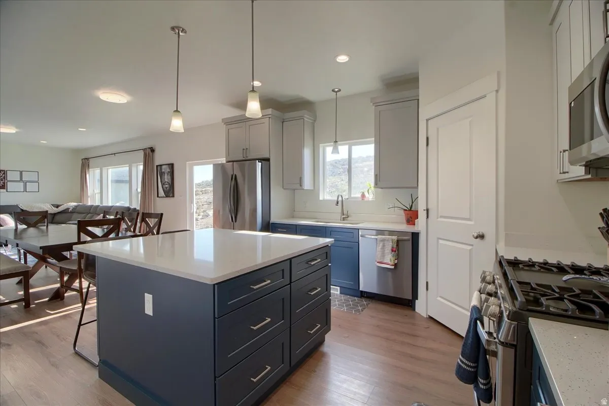 Kitchen featuring an island with stone countertops, stainless steel appliances, pendant lighting, and wood-finish flooring