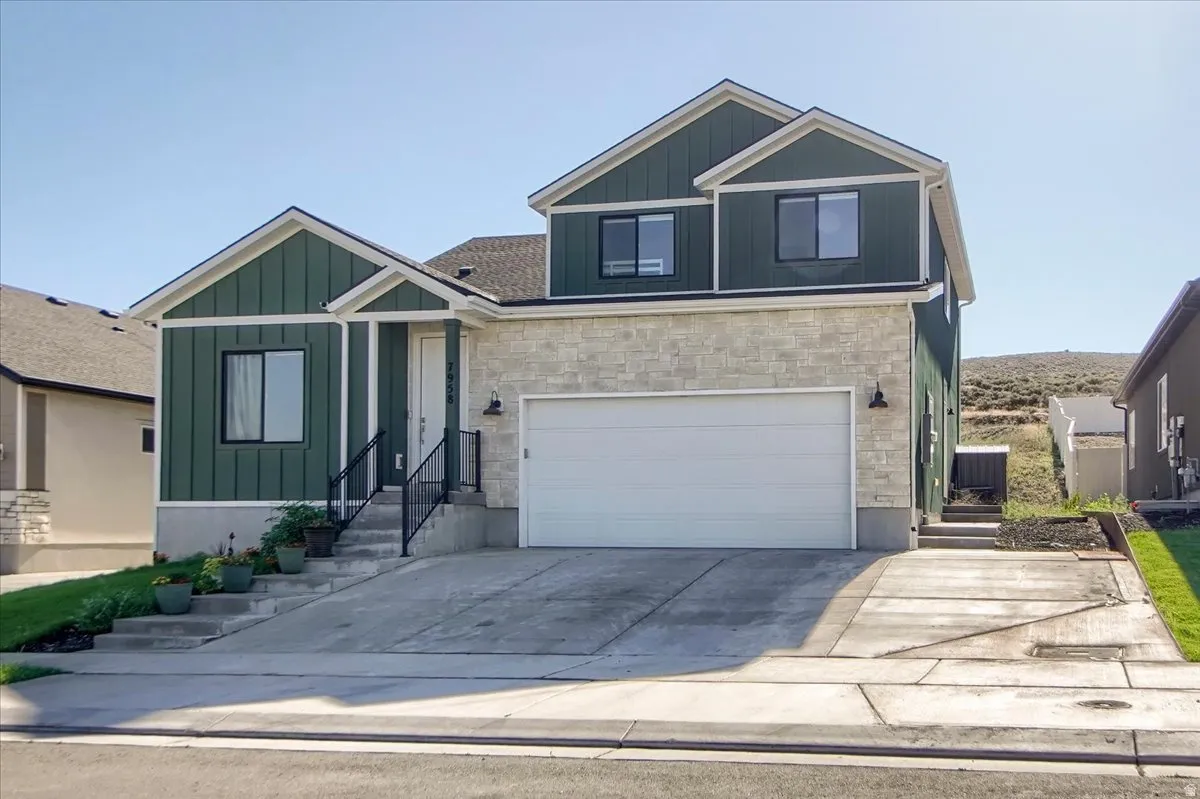 Contemporary multi-level residence featuring dark green vertical siding, light-colored stone veneer, a two-car garage with a white door, and a concrete driveway