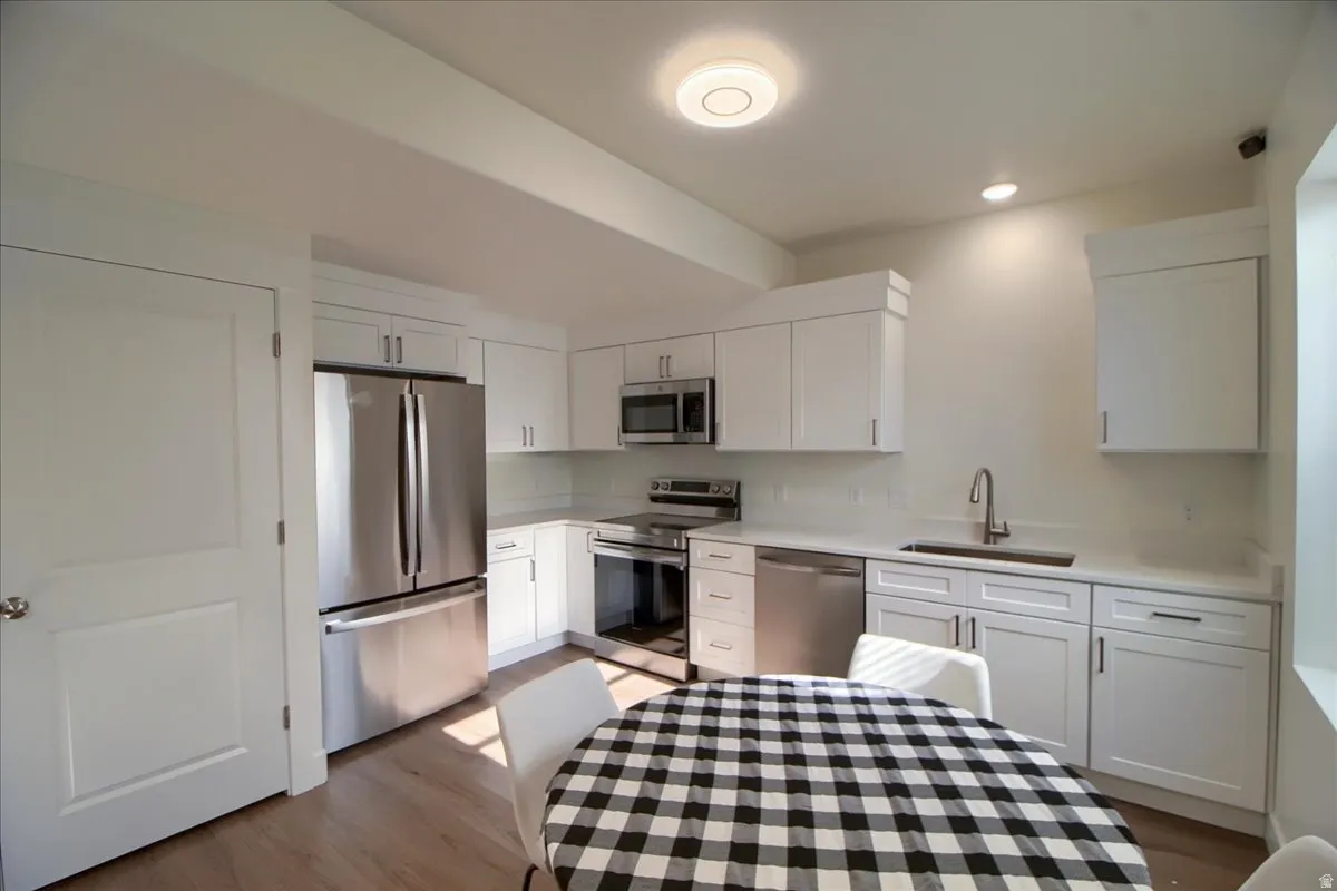 Contemporary kitchen featuring white cabinetry, stainless steel appliances, light-toned countertops, subway tile backsplash, and wood-finish flooring